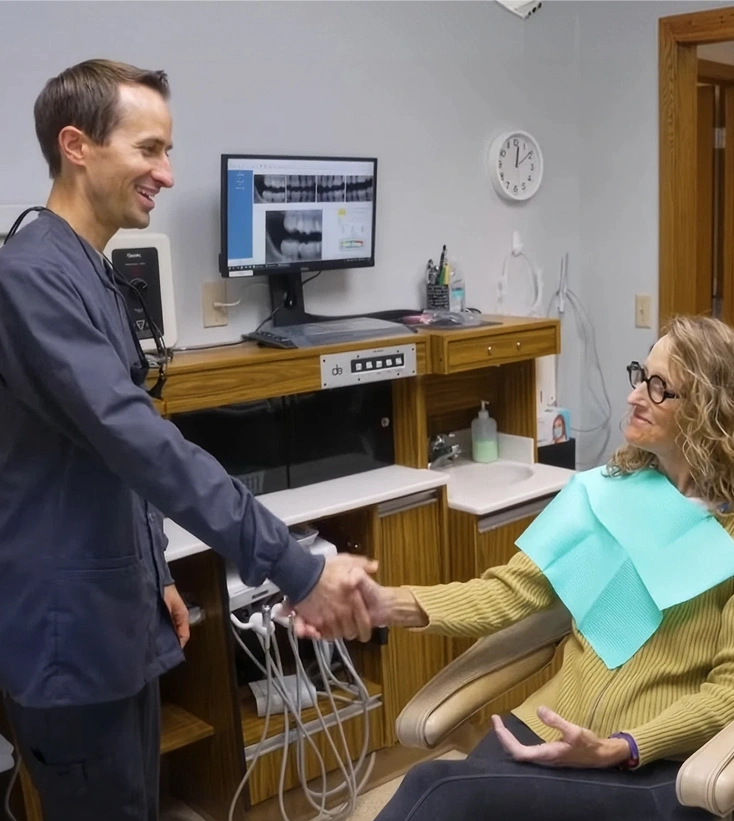 Dentist shaking hands with a smiling patient seated in a dental chair