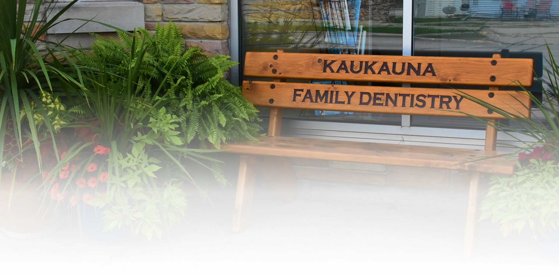 Kaukauna Family Dentistry wooden bench surrounded by lush greenery and flowers outside the dental office in Kaukauna, Wisconsin